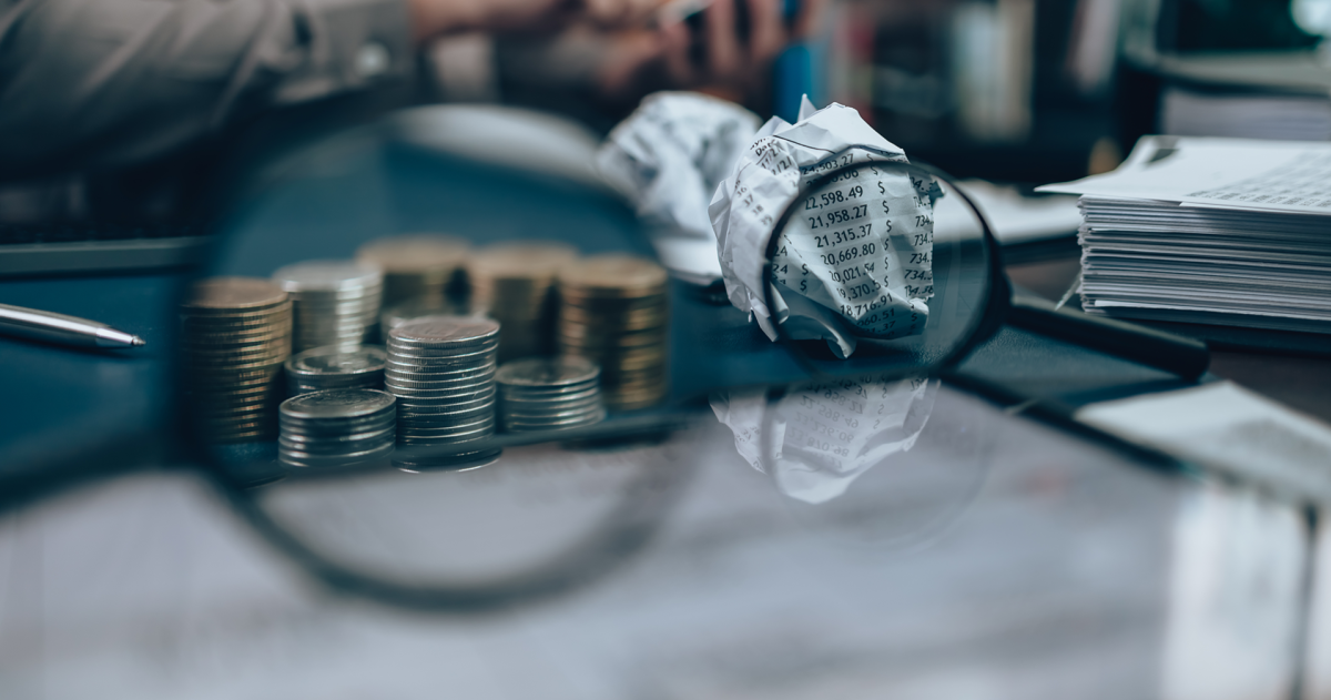 Vergrootglas vergroot een stapel munten en een prop paier met allerlei kosten erop